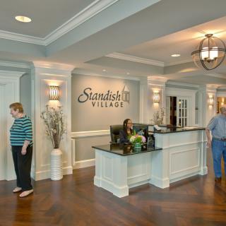 A reception area with a sign that reads 'Standish Village', featuring a front desk and several people in an elegantly designed interior.