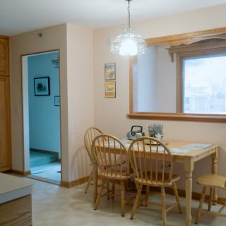 A cozy kitchen dining area with a wooden table and chairs, illuminated by natural light from a nearby window.