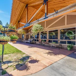 A modern building with an extended wooden roof and outdoor patio area, surrounded by greenery on a sunny day.