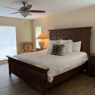 A cozy bedroom featuring a large wooden bed, ceiling fan, and soft natural lighting.