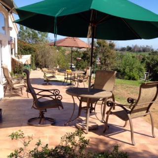 A sunny patio with outdoor furniture and a green umbrella.