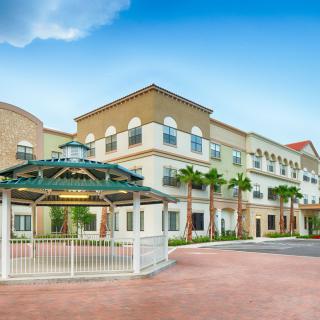 A modern, multi-story building with palm trees and a gazebo under a clear blue sky.
