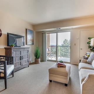 A cozy living room with modern furniture, featuring a sofa, TV stand, and coffee table. Large windows open to a balcony with outdoor views.