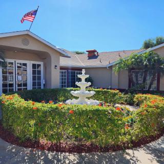 A peaceful garden with a central fountain in front of a building, adorned with an American flag on a sunny day.