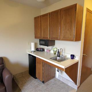 A small kitchenette with wooden cabinets, a sink, and a mini fridge.