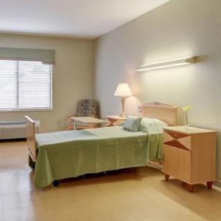 A clean and minimalist hospital room with a single bed, side tables, and a lamp.