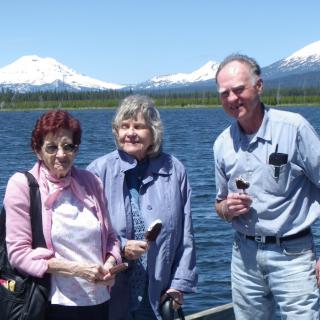 Three people enjoying a scenic view by a lake with mountains in the background.