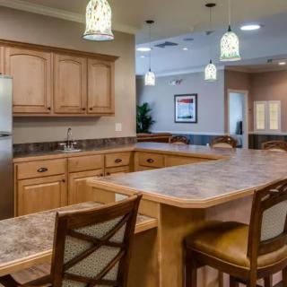 A modern kitchen with wooden cabinets and a marble countertop, featuring pendant lights and bar stools.