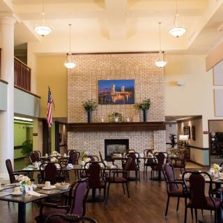 A spacious dining area with neatly arranged tables and chairs, featuring a central fireplace and elegant decor.