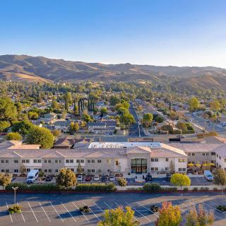 Aerial view of a suburban area with buildings and a parking lot, surrounded by hills and greenery.
