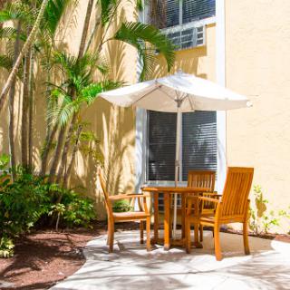 A cozy outdoor seating area with a table and chairs under an umbrella, surrounded by lush greenery.