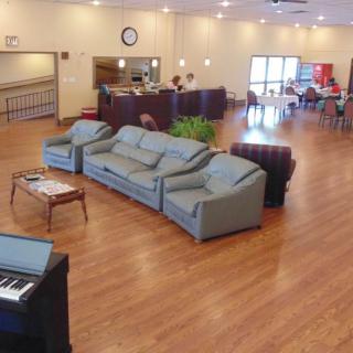 A spacious indoor lounge area featuring comfortable sofas, a piano, and wooden flooring.