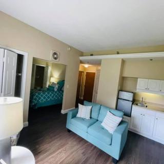 A modern apartment with a cozy living room, featuring a blue couch and kitchenette adjacent to a bedroom.