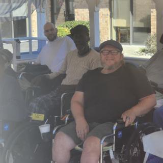A group of individuals enjoying a sunny day outdoors, gathered in wheelchairs.