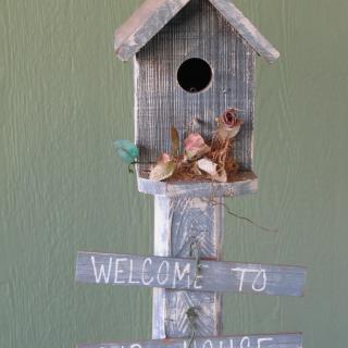A charming rustic birdhouse with a welcome sign attached.