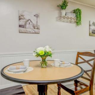 A cozy dining area with a round table set for two, featuring floral decor and wall art.