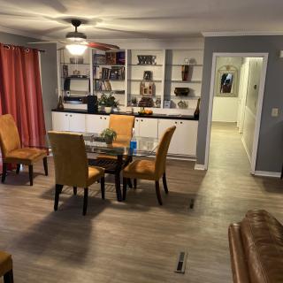 A cozy dining room with a glass table and chairs, surrounded by decorative shelves and vibrant curtains.