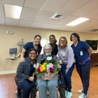 A heartfelt moment of celebration with a patient surrounded by dedicated healthcare staff and beautiful flowers.