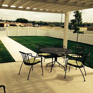 A cozy patio setup with metal table and chairs under a pergola, overlooking a well-maintained lawn and garden.