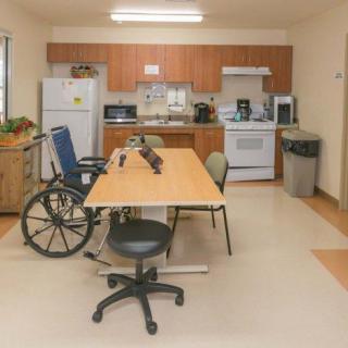 A kitchen setup with a table, chairs, and a wheelchair indicating an accessible space.
