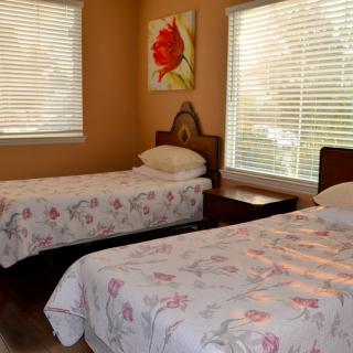 A cozy bedroom with two twin beds featuring floral bedding, complemented by a nightstand and artwork on the wall.