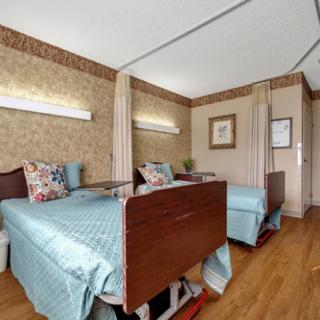 A hospital room with two patient beds separated by curtains and a wooden floor.