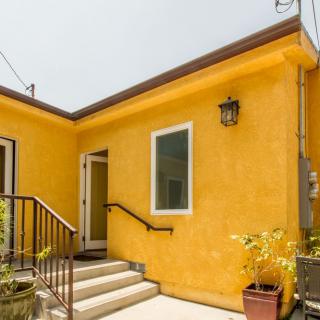 A small yellow stucco house with steps leading to the entrance, featuring potted plants and a lantern.