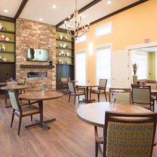 A modern dining area with wooden tables, upholstered chairs, a stone fireplace, and a chandelier.
