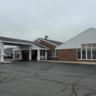 A large building with a covered entrance and adjacent parking area on an overcast day.