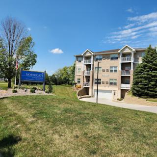 A modern apartment building surrounded by lush greenery under a bright blue sky.
