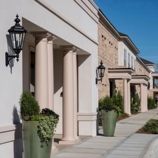 A row of buildings with classical columns and decorative lamps flanking a sidewalk on a sunny day.
