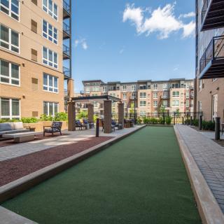 A modern apartment courtyard featuring a bocce court and seating areas surrounded by tall buildings.