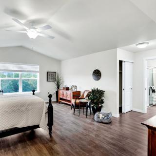 A spacious bedroom with wooden flooring, featuring a bed, ceiling fan, and stylish decor.
