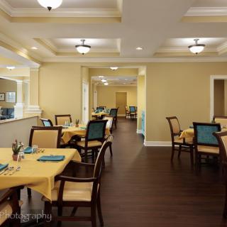 A well-lit dining room with neatly arranged tables and chairs, featuring yellow tablecloths and modern lighting.