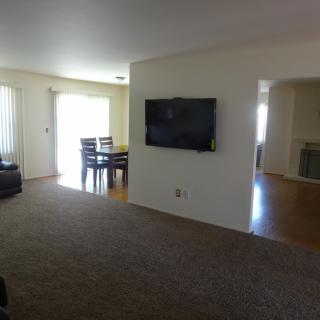 A spacious living room with a television on the wall, adjacent to a dining area featuring wooden floors.