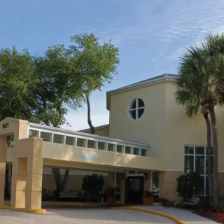 The image shows an entrance to a building surrounded by trees and palm trees on a clear day.