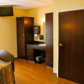A cozy hotel room with wooden flooring, a wardrobe, and a television mounted on the wall.