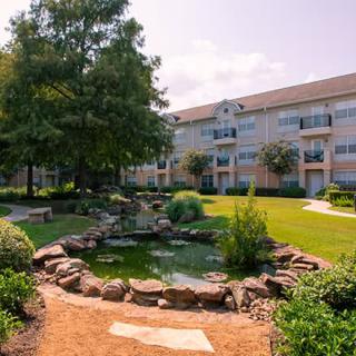 A beautifully landscaped apartment complex featuring a serene pond and lush greenery.