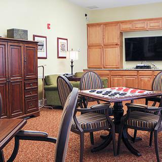 A cozy living room featuring a table with a checkers board, surrounded by chairs and an entertainment center with a TV.