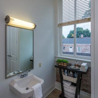 A small bathroom with a sink, mirror, and window overlooking a building.