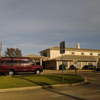 A red van parked in front of a multi-story building under a cloudy sky.