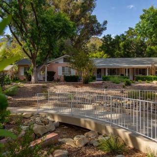 A serene house surrounded by lush trees, featuring a small bridge in the garden.