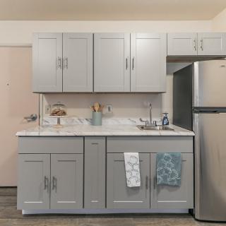 A modern kitchen with gray cabinets, a countertop with utensils and towels, and a stainless steel refrigerator.