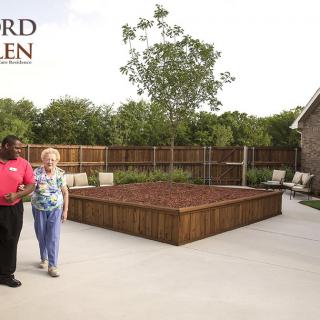 Two people walking in a well-maintained garden area, surrounded by seating and greenery.