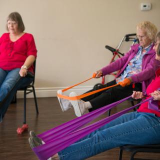 A group of seniors participating in a chair exercise class using resistance bands.