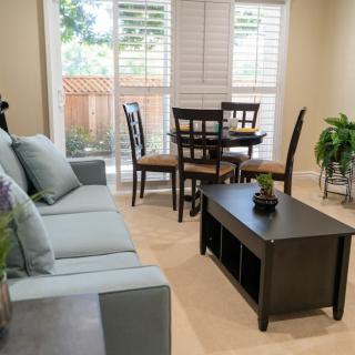 A cozy living room with a sofa, coffee table, and dining area featuring natural light from large windows.