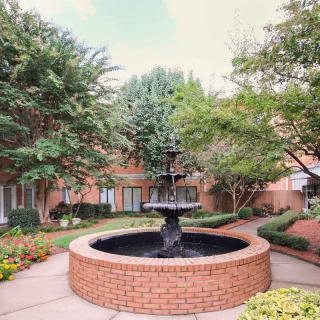A tranquil courtyard featuring a central brick fountain surrounded by lush trees and landscaped pathways.