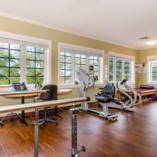 A well-lit rehabilitation gym with exercise equipment and large windows.