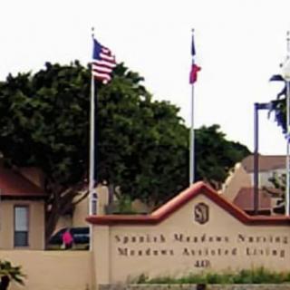 Entrance sign of Spanish Meadows Nursing & Assisted Living with flags and trees in the background.