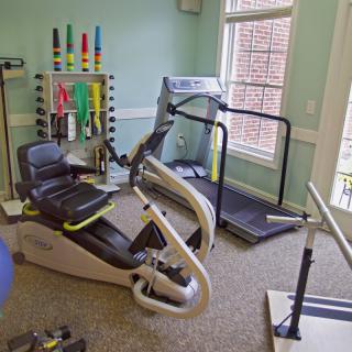 A small gym with various exercise equipment, including a treadmill and a stationary bike, in a well-lit room.